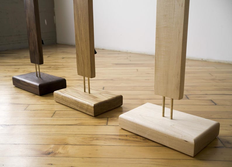 May include: Three wooden sculptures with rectangular bases and vertical posts. The sculptures are made of different types of wood, including dark brown, light brown, and natural wood. The posts are supported by brass rods.