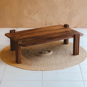 May include: A rectangular low-profile coffee table crafted from dark brown wood with a smooth surface. The table features four thick, vertically ribbed legs and distinct joinery details where the legs meet the tabletop corners.