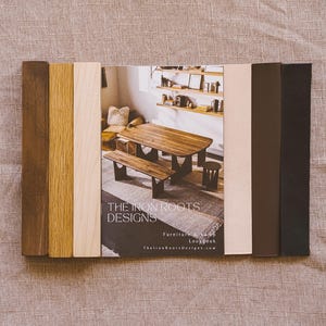 May include: A furniture catalog featuring a wooden table and bench set, with a small stool. The catalog is flanked by wooden color swatches in shades of brown, tan, and beige. The catalog reads "THE IRON ROOTS DESIGNS".