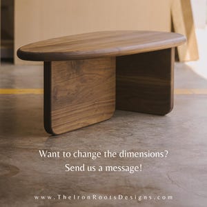 May include: A wooden coffee table with a smooth, oval top and two rectangular legs. The table is made of dark brown wood with visible grain. Text on the image reads: "Want to change the dimensions? Send us a message!"