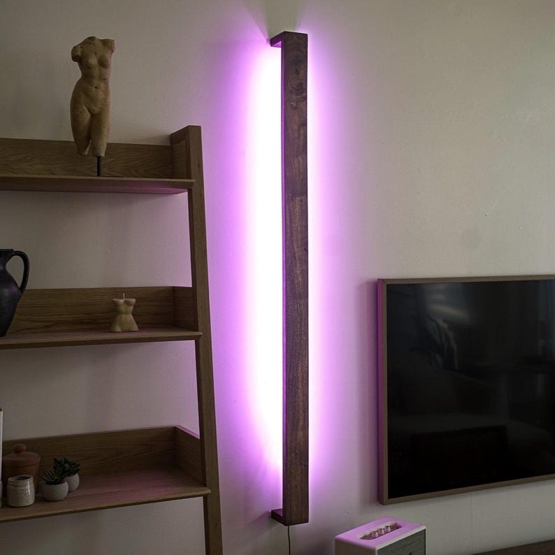 Puede incluir: Una l&aacute;mpara de pared vertical de madera con una luz rosa brillante. La l&aacute;mpara est&aacute; montada en una pared blanca, junto a una estanter&iacute;a de madera y un televisor. El marco de madera de la l&aacute;mpara es de color marr&oacute;n oscuro. La l&aacute;mpara mide unos 180 cm de alto.