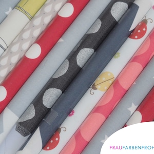 Könnte beinhalten: Eine Sammlung gerollter Stoffballen in verschiedenen Farben und Mustern. Designs umfassen Punkte, Marienkäfer, Sterne und Tropfen. Die Farben reichen von Rot und Rosa bis Grau und Blau. Das Bild enthält den Text "FRAUFARBENFROH."