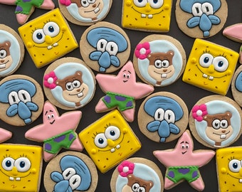 May include: A collection of colorful, cartoon-themed sugar cookies. The cookies feature characters like SpongeBob SquarePants, Patrick Star, Squidward Tentacles, and Sandy Cheeks. The cookies are decorated with intricate details and bright colors.