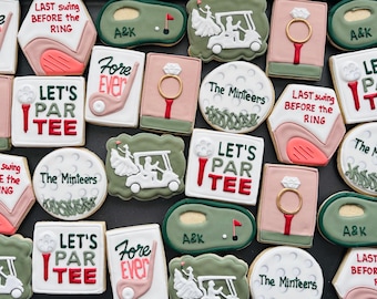 May include: Assortment of decorated sugar cookies with golf and wedding themes. Designs include golf clubs, golf carts, rings, and phrases like "Fore Ever" and "Let's Par Tee." Colors are white, pink, green, and red.