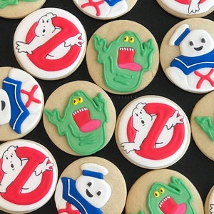 May include: A collection of Ghostbusters-themed sugar cookies decorated with various characters and symbols, including the Ghostbusters logo, Slimer, and Stay Puft Marshmallow Man.