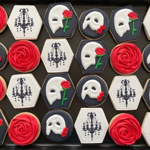 May include: A collection of 18 decorated sugar cookies featuring a phantom of the opera theme. The cookies are decorated with red roses, a chandelier, and a white mask with a black background.