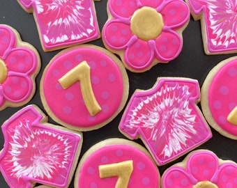 May include: Pink and white decorated sugar cookies with a tie-dye design, a flower design, and the number 7.