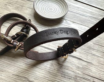 May include: Two brown leather dog collars, one with a silver buckle and the other with a gold buckle. The larger collar has the text "Lucky Dog" embossed on it.