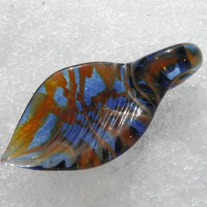 May include: A blue and orange glass pendant shaped like a leaf with swirls of colour.