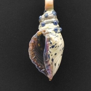 May include: A glass seashell pendant necklace with a white, brown, and blue swirl pattern. The pendant has a small hole at the top for attaching a cord or chain.