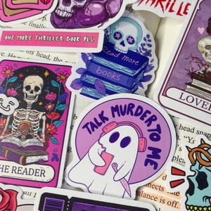 May include: A collection of stickers with a thriller theme. Designs include skulls, hearts, tarot cards, ghosts, and books. Text on the stickers includes "Thriller Book Club" and "Talk Murder to Me."