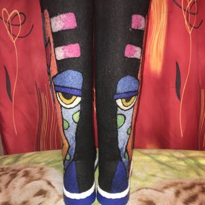Puede incluir: Un par de botas de fieltro negro con diseños abstractos coloridos, incluyendo azul, verde, amarillo, rosa y naranja. Las botas tienen un ribete blanco alrededor de las suelas y suelas azules.
