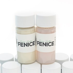 May include: Two small bottles of leather paint with white caps. One bottle contains a cream-colored paint, and the other contains a light pink paint. The bottles have labels with the text "Loving Leather FENICE".