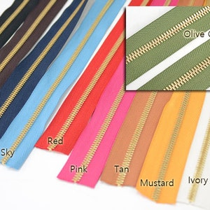 Puede incluir: Una colecci&oacute;n de cremalleras coloridas en varios tonos, incluyendo negro, marr&oacute;n oscuro, azul marino, celeste, rojo, rosa, beige, mostaza, marfil y blanco. Cada cremallera tiene un tirador y dientes de metal dorado. Tambi&eacute;n se muestra un primer plano de una cremallera verde oliva.