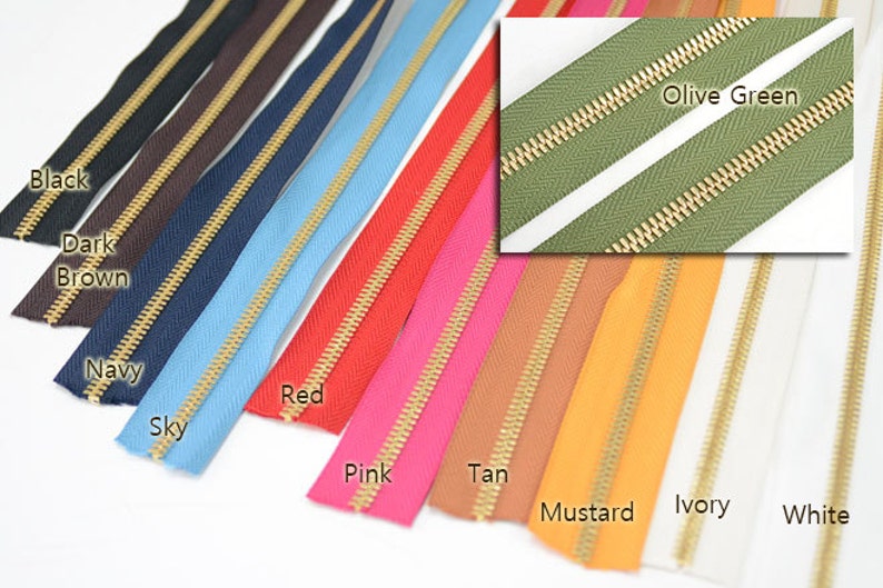 Puede incluir: Una colecci&oacute;n de cremalleras coloridas en varios tonos, incluyendo negro, marr&oacute;n oscuro, azul marino, celeste, rojo, rosa, beige, mostaza, marfil y blanco. Cada cremallera tiene un tirador y dientes de metal dorado. Tambi&eacute;n se muestra un primer plano de una cremallera verde oliva.