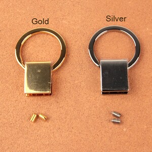 Pu&ograve; includere: Due pezzi di ferramenta per portachiavi in metallo, uno dorato e uno argentato, ciascuno con una base rettangolare e un anello circolare. Sono incluse piccole viti. Le parole "Gold" e "Silver" sono stampate sopra.