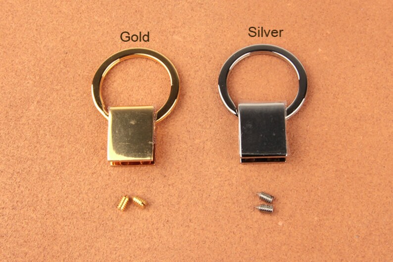 Pu&ograve; includere: Due pezzi di ferramenta per portachiavi in metallo, uno dorato e uno argentato, ciascuno con una base rettangolare e un anello circolare. Sono incluse piccole viti. Le parole "Gold" e "Silver" sono stampate sopra.