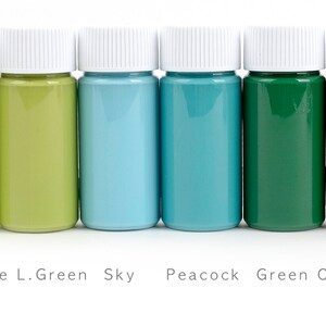 May include: Six small paint bottles with white lids, showcasing a spectrum of colors from light green to dark olive green. The labels read: fluorescence L.Green, Sky, Peacock, Green, and Olive Green.
