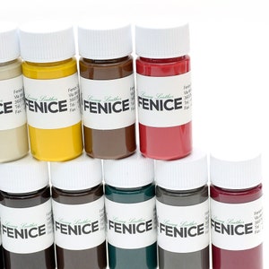 May include: A collection of small, colorful bottles of leather paint. The bottles are arranged in a group, showcasing a variety of hues including yellow, brown, red, and green. Each bottle has a white cap and a label with the word "FENICE".