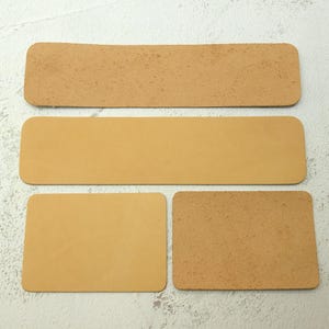 Puede incluir: Cuatro piezas rectangulares de cuero color canela dispuestas sobre un fondo claro. Dos piezas son largas y estrechas, mientras que las otras dos son más cortas y anchas. Una de las piezas cortas tiene una superficie rugosa y texturizada.