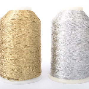 Puede incluir: Dos bobinas de hilo metálico, una dorada y otra plateada, sobre fondo blanco. El hilo está enrollado apretadamente alrededor de una base de plástico blanco. Ideal para bordado y costura. Las bobinas están una al lado de la otra.