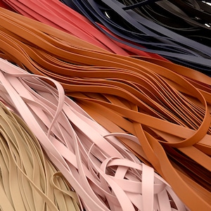 May include: A close-up shot of several leather strips in various colors. The colors include tan, light pink, brown, red, and navy blue. The strips are arranged in a slightly chaotic, overlapping pattern.