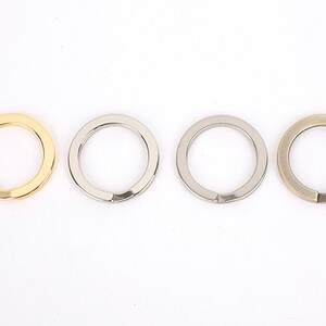 Può includere: Quattro portachiavi in metallo nei toni oro, argento e bronzo. Ogni anello è circolare con un'apertura divisa per attaccare chiavi o altri oggetti. Gli anelli sono esposti su sfondo bianco.