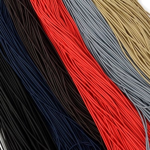 May include: A close-up view of several bundles of elastic cord in various colors. The colors include black, navy blue, brown, red, gray, and tan. The cords are tightly packed together, creating a textured surface.