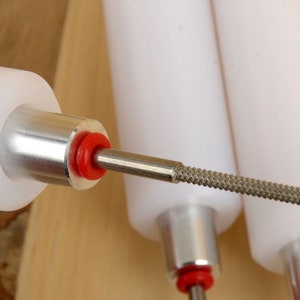 May include: Close-up of three white and silver tools with red accents. The tools have a cylindrical white body, a silver metal base, and a textured, gray metal tip. The tools are likely used for precision work.