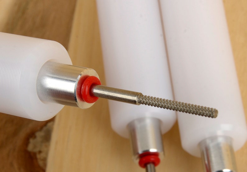 May include: Close-up of three white and silver tools with red accents. The tools have a cylindrical white body, a silver metal base, and a textured, gray metal tip. The tools are likely used for precision work.