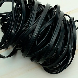 May include: A close-up of a tangled mass of black rubber strips. These strips appear to be for sealing or edging purposes. The material is smooth and flexible, with a subtle sheen. The image highlights the texture and form of the rubber.