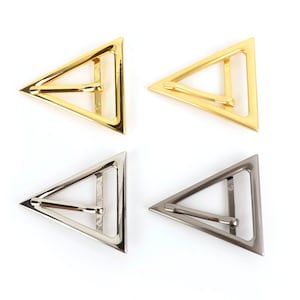 Op de afbeelding: Vier metalen driehoekige gespen in goud- en zilverkleuren. Elke gesp heeft een driehoekig frame met een horizontale balk in het midden. De gespen worden weergegeven tegen een witte achtergrond.