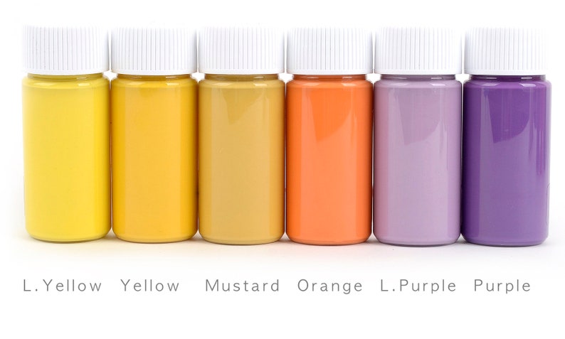 May include: Six small bottles of paint in a row, each filled with a different color. The colors are yellow, mustard, orange, light purple, and purple. Each bottle has a white cap, and the names of the colors are printed below.