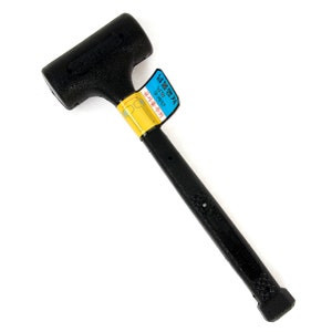 May include: A black rubber mallet with a textured handle and head. The mallet has a label with Korean text attached to the handle. The head of the mallet is rectangular and the handle is cylindrical.