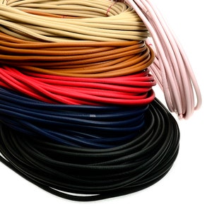 May include: A collection of colorful leather cords in various shades, including tan, brown, red, navy, and black. The cords are coiled and appear to be new. A light pink cord is also visible.