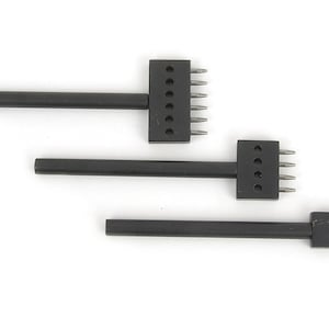 Può includere: Tre strumenti neri per la lavorazione della pelle con punte metalliche. Gli strumenti sono disposti in fila, ciascuno con un numero diverso di punte. Gli strumenti servono a creare fori nella pelle per cucire o per altri scopi.