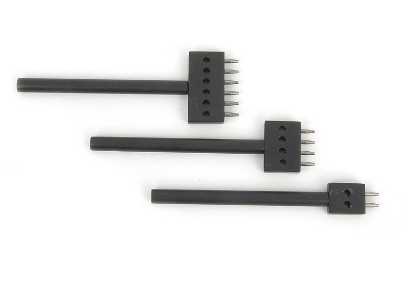 May include: Three black leather working tools with metal prongs. The tools are arranged in a row, each with a different number of prongs. The tools are used for creating holes in leather for stitching or other purposes.