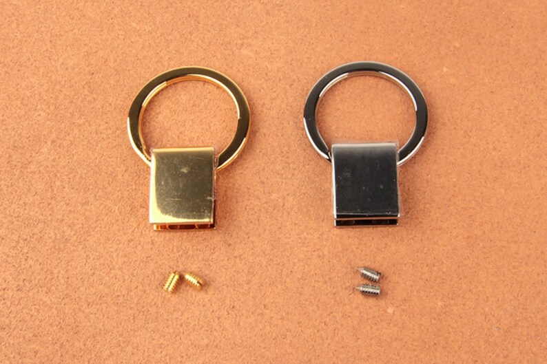 Pu&ograve; includere: Due anelli metallici, uno dorato e uno argentato, con chiusure rettangolari. Sono incluse piccole viti. Probabilmente utilizzati per la fabbricazione di borse o altri progetti artigianali.