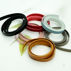 May include: A collection of coiled leather strips in various colors, including black, red, pink, gray, and brown. The strips are thin and appear to be made of genuine leather, suitable for crafting or jewelry making.