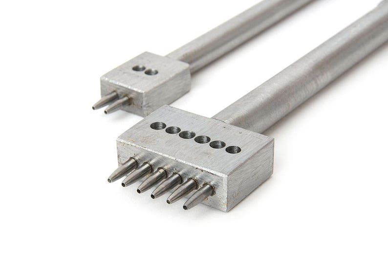 May include: Two silver leather working tools with multiple prongs. One tool has two prongs, and the other has six. The tools are made of metal and are designed for punching holes in leather.