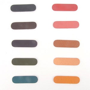 May include: A collection of leather swatches in various colors, including dark gray, red, pink, brown, olive green, teal, and orange. Each swatch is a small, rectangular shape with rounded ends, displayed against a white background.