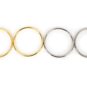 Könnte beinhalten: Vier kreisförmige Metallringe, zwei goldfarbene und zwei silberfarbene, vor weißem Hintergrund. Die Ringe haben eine glatte, polierte Oberfläche. Die goldenen Ringe sind links, die silbernen rechts.