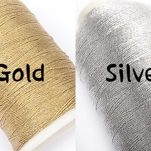 May include: Two spools of metallic thread, one gold and one silver, are displayed against a white background. The word "Gold" is written in black on the gold spool, and "Silver" is written on the silver spool.
