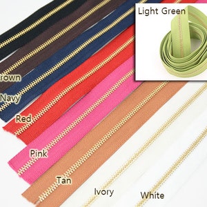 Puede incluir: Una variedad de cremalleras de colores con dientes dorados. Los colores incluyen negro, marr&oacute;n oscuro, azul marino, rojo, rosa, beige, marfil y blanco. Una inserci&oacute;n separada muestra una cremallera verde claro.