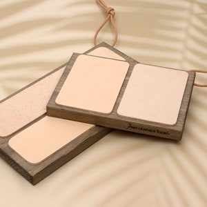 Puede incluir: Tres badanas de madera para trabajar el cuero con superficies de cuero marrón claro. Las bases de madera son rectangulares con un acabado gris oscuro. Cada badana tiene una superficie de cuero, lisa o texturizada. Una cuerda de cuero está unida a cada badana.