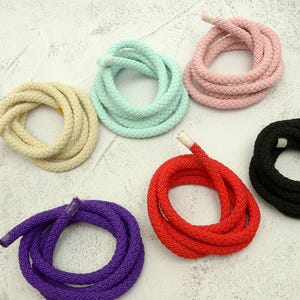 May include: Coiled ropes in various colors: yellow, mint green, pink, black, red, and purple. The ropes are made of a thick, woven material. The ends of the ropes are finished with a white tip. The ropes are arranged in a circular pattern.