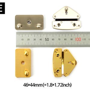 May include: Various metal hardware pieces, including rectangular and triangular shapes, are displayed with a ruler for size comparison. The pieces are gold and silver-toned, with screw and keyhole details. The dimensions are 1.8 x 1.72 inches.