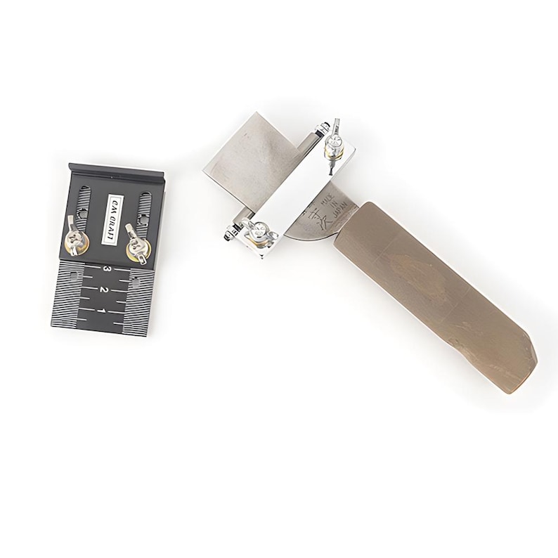May include: A set of woodworking tools, including a blade sharpener with a wooden handle and a black metal measuring guide. The blade sharpener has a silver blade and white support. The measuring guide has the text "CM CRAFT".