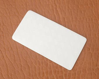 Puede incluir: Una tarjeta blanca rectangular en blanco con esquinas redondeadas descansa sobre una superficie marrón texturizada. La tarjeta está colocada en diagonal, ocupando una parte importante del encuadre. La superficie tiene un patrón ondulado.