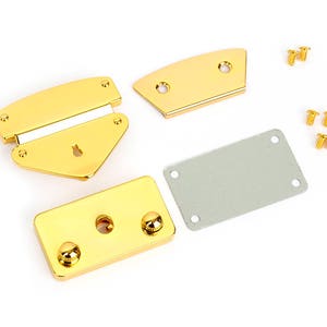 May include: A set of gold-colored metal purse hardware components, including a clasp, two curved pieces, a rectangular plate, and small screws. The hardware is new and shiny, ideal for crafting or repair projects.